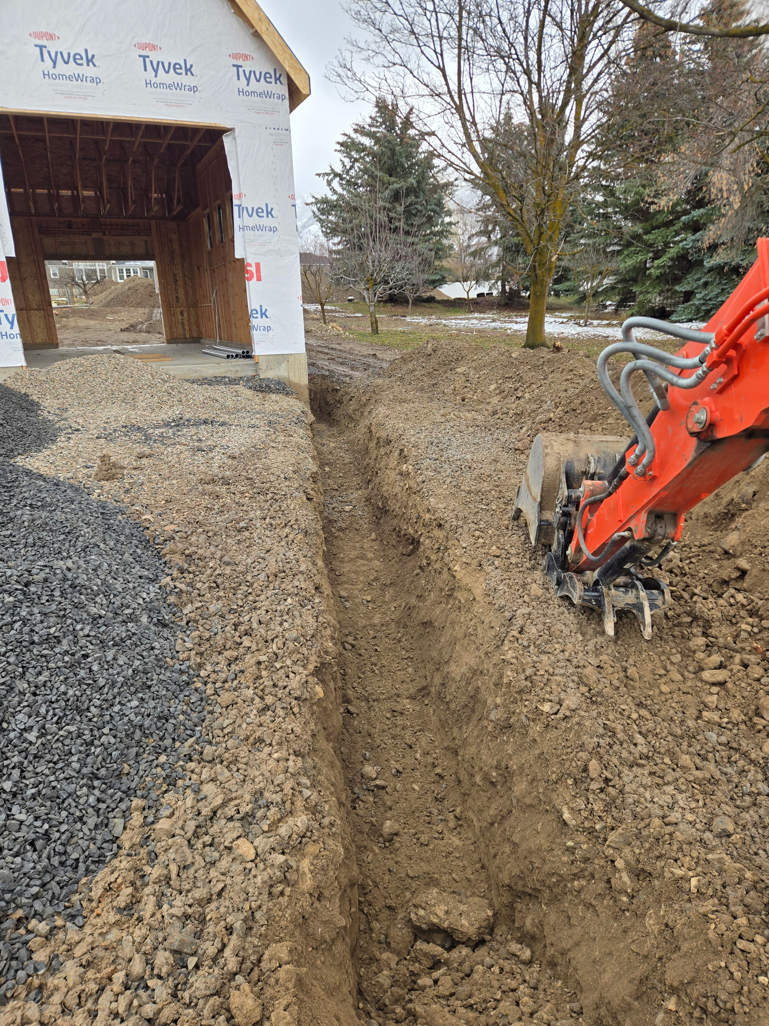 Excavator trenching next to new construction